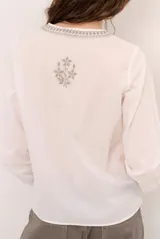 Blusa celeste de manga larga con delicados bordados florales en tono más claro en la zona del pecho y mangas. Presenta escote en V y puños elásticos abotonados.