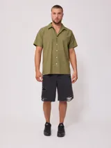 Camisa de manga corta color negro, con cuello camisero y botones blancos frontales.