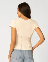 Remera blanca de manga corta con cuello redondo, confeccionada en una mezcla de modal, poliéster y elastano. Presenta un diseño con alforzas verticales en el frente que aportan estructura y una silueta relajada.
