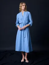 Vestido maxi color beige, con cuello mao y escote en V. Presenta mangas largas con presilla y botón para regular el largo, y un lazo ajustable en la cintura que marca la silueta.