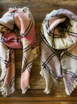 Bufanda rectangular con estampado a cuadros en tonos rosa, beige y negro, con flecos en los extremos.