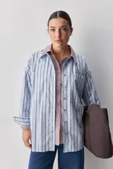Camisa de calce relajado con diseño a rayas verticales en tonos azul y blanco, cuello clásico, mangas largas con puños abotonados y cierre frontal con botones. Presenta bolsillos aplicados en el delantero y una silueta versátil.