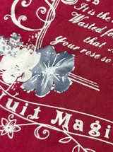 Remera bordó de manga corta con diseño de hombros descubiertos (off-shoulder) y un detalle superpuesto tipo bikini negro en el cuello. Cuenta con un estampado gráfico frontal de estilo vintage con flores y texto.