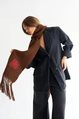 Bufanda de algodón color marrón con flecos en los extremos y logo bordado en amarillo.