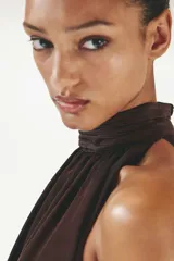 Cropped top halter de color marrón oscuro con leve brillo, escote alto con cuello elevado fruncido y diseño abullonado en el bajo.