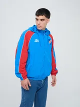 Campera deportiva Umbro del Club Nacional de Football, modelo Venti, para hombre. Diseño en color blanco con mangas azules y detalles de líneas rojas. Cuenta con capucha con cordón ajustable, cierre frontal y bolsillos. Presenta el logo de Umbro y el escudo del club bordados en el pecho.