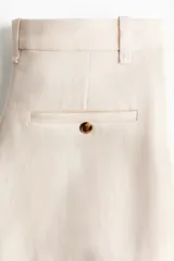Pantalón sastrero color beige, de corte amplio y recto, con pinzas en la parte delantera y cierre frontal con botón.