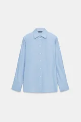Camisa de manga larga con cuello solapa y hombreras. Presenta un diseño de rayas verticales en tonos azul y blanco, con cierre frontal de botones y puños anchos.