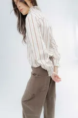 Camisa de corte clásico con estampado de rayas verticales, cuello alto con volados frontales y mangas largas con puños con volados.