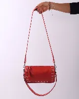 Bandolera de cuero natural color rojo, con diseño rectangular y detalles de tachas metálicas en los laterales y en la correa. Cuenta con cierre superior y dos asas desmontables.