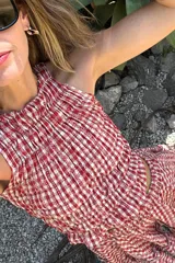 Top sin mangas con cuello alto y diseño fruncido elástico en toda la prenda. Presenta un estampado de cuadros vichy en color rojo y blanco con detalles bordados.