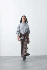 Polera de tejido de punto color gris, con cuello alto, mangas largas abullonadas con puños elásticos y costura central vertical en el frente. Presenta una abertura sutil en la espalda.
