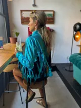 Campera turquesa de tela brillante con flecos en mangas y ruedo.