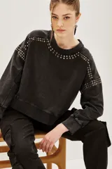 Buzo de algodón color negro con efecto lavado, corte holgado y detalles de tachas metálicas plateadas alrededor del cuello redondo y en los hombros.