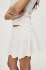 Falda corta blanca con diseño de volados escalonados y cintura elastizada, de silueta fluida y liviana.