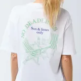 Camiseta blanca de corte oversize, con mangas cortas y cuello redondo, presenta un pequeño estampado gráfico en el pecho con la frase 'Sun & Limes'.
