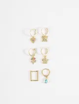 Set de seis aros tipo argolla dorados con dijes colgantes variados: un corazón con ojo turco, una mariposa, un trébol de cuatro hojas con piedras de colores, una flor, un rectángulo con piedras y una gota de cristal turquesa.