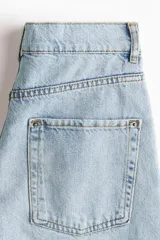 Jean de cinco bolsillos en denim de algodón rígido, corte holgado con cierre y botón. Cuenta con piernas amplias de diseño curvado, raya marcada y bajo deshilachado.