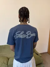 Remera de algodón color azul con estampa gráfica blanca en el pecho y etiqueta pequeña en la manga.