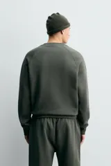 Sudadera de corte relajado confeccionada en algodón compacto con interior de rizo. Presenta cuello redondo, mangas largas tipo raglán y terminaciones en rib.