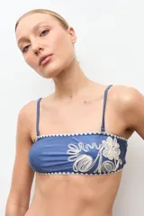 Top de bikini bandeau color azul con detalle de bordado floral en hilo crudo en el lateral.