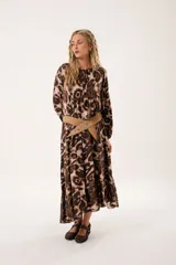 Vestido midi de corte holgado con estampado animal print en tonos marrones y beige. Tiene cuello redondo con lazo, mangas largas abullonadas y falda amplia con volantes. Incluye cinturón marrón con tachas.