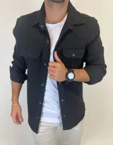 Sobrecamisa de gabardina color negro, con cierre frontal de botones metálicos a presión, bolsillos frontales con solapa y mangas largas.
