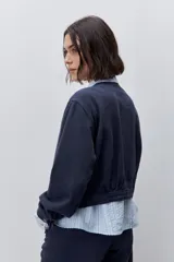 Campera azul marino de algodón, de corte relajado y largo corto, con cuello redondo, cierre frontal con botones metálicos, bolsillos delanteros y mangas largas con puños ajustables.