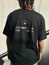 Remera negra de corte oversize con estampado en la espalda que dice 'REAL ADVENTURE STORIES OF THE EAST'.