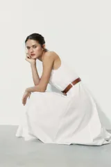 Vestido midi de color blanco con escote cuadrado y tirantes finos. Presenta un diseño acampanado con pliegues y un cinturón de cuero sintético en color tostado con hebilla metálica dorada.
