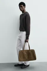 Bolso de viaje tipo duffel de piel con acabado serraje, color verde oliva. Presenta dos asas de mano y un compartimento principal con cierre de cremallera e imanes. El interior incluye un bolsillo con cremallera y un bolsillo plano.