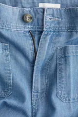 Pantalón de jean de denim rígido, color celeste claro, tiro alto, pierna amplia y corte holgado. Presenta pliegues frontales y traseros, cierre con botón y bolsillos parche en la parte delantera y trasera.