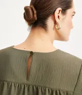 Blusa de poliéster color verde oliva, con cuello redondo, manga corta y detalle de pliegues fruncidos en la costura de los hombros.