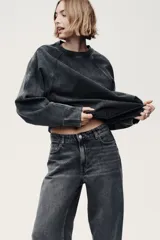 Jean de corte baggy, estilo holgado con piernas rectas, confeccionado en denim de algodón color gris oscuro con efecto lavado. Cuenta con tiro estándar, trabillas para cinto, cierre frontal con botón y cinco bolsillos clásicos.