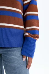 Buzo de punto con diseño de rayas horizontales en tonos azul, marrón y blanco. Presenta cuello redondo, mangas largas y puños anchos acanalados.