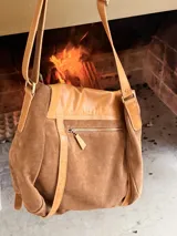 Bandolera tipo messenger bag confeccionada artesanalmente en combinación de cuero y gamuza marrón. Cuenta con solapa frontal de cuero con broches a presión, correas decorativas con hebillas metálicas y una correa larga ajustable para el hombro. Incluye parche con logo grabado en la parte frontal.