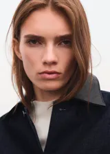 Chaqueta de denim en color azul oscuro, con diseño recto, cuello camisero, cierre frontal de botones metálicos y bolsillos de parche con solapa en el pecho.