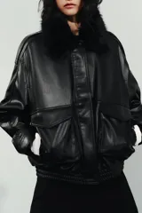 Cazadora de cuero sintético en color negro, con cuello de solapa y aplicación de pelo sintético desmontable. Presenta cierre frontal con cremallera y botones a presión ocultos, bolsillos de plastrón con solapa en el delantero y bajo con elástico.