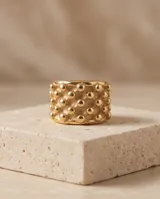 Anillo ancho de acero con baño de oro, con diseño de textura punteada en relieve.