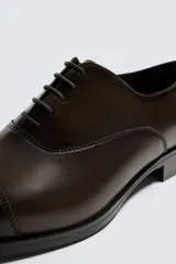 Zapato de vestir tipo Oxford en color negro, con diseño de puntera reforzada y cierre mediante cordones. Presenta una silueta clásica y elegante con tacón bajo.