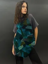 Poncho de lana merino afieltrada con cuello alto y mangas cortas. Diseño tipo mosaico con piezas geométricas en tonos verde azulado y gris.