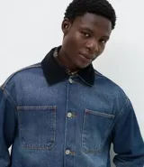 Campera de jean de corte oversized, con cuello de terciopelo, cierre frontal por botones y bolsillos grandes aplicados en el frente.