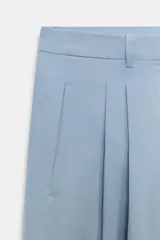 Pantalón wide leg de tiro medio confeccionado en hilatura de algodón, color beige, con trabillas en la cintura, bolsillos laterales ocultos y detalle de pliegues en el delantero. Cierre frontal con cremallera, botón y ganchos metálicos.