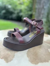 Sandalias de cuero color marrón chocolate con plataforma y taco corrido. Tira ancha sobre los dedos y tira al tobillo con hebilla dorada.