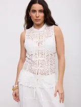 Top de encaje color blanco, sin mangas, con cuello mao y cierre frontal con nudos y presillas.