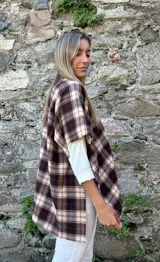 Ruana estilo chaqueta con diseño de cuadros escoceses en tonos marrones y beige. Presenta un cierre frontal tipo alamar con detalle en cuero sintético y bordes terminados.