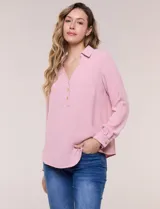 Blusa holgada de crepé rosado, con cuello camisero, escote en V y cierre frontal parcial de tres botones metálicos. Cuenta con mangas largas convertibles en tres cuartos mediante presilla.