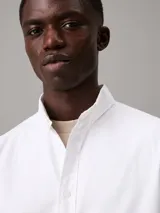 Camisa blanca de corte regular, confeccionada en tejido oxford de algodón y elastano. Tiene mangas largas con puños abotonados, cierre frontal con botones y cuello clásico. Incluye etiqueta con el logo de Calvin Klein.