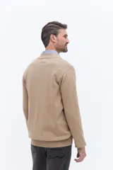 Campera de tejido de punto liviano color beige, con cierre frontal completo y cuello alto tipo bomber. Presenta un pequeño logo bordado en el pecho y puños acanalados.