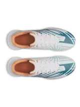 Championes de fútbol Under Armour Shadow Club 4 Turf, diseñados para césped artificial. Presentan un diseño en color blanco con detalles gráficos en azul y toques en naranja. Cuentan con empeine sintético, cordones centrales y suela de goma con tacos multidireccionales para un agarre óptimo.